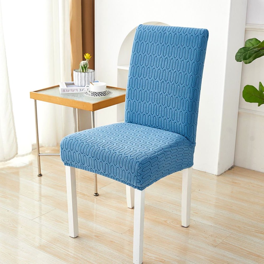 Funda elástica de jacquard para silla, color azul océano, con patrón de chevrón en laberinto, mostrada en una silla de comedor en un ambiente moderno con mesa auxiliar y planta.