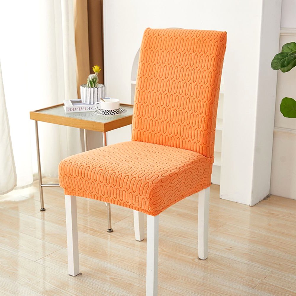 Funda elástica de jacquard para silla, color naranja atardecer, con patrón de chevrón en laberinto, mostrada en una silla de comedor en un ambiente moderno con mesa auxiliar y planta.
