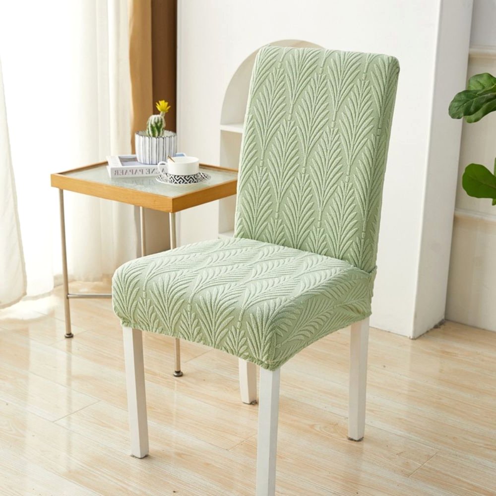 Funda elástica de jacquard Velvet Haven para silla, color verde salvia, con patrón de palma tejida, mostrada en una silla de comedor blanca. Este protector de muebles de ajuste elástico ofrece un diseño moderno y fácil instalación.