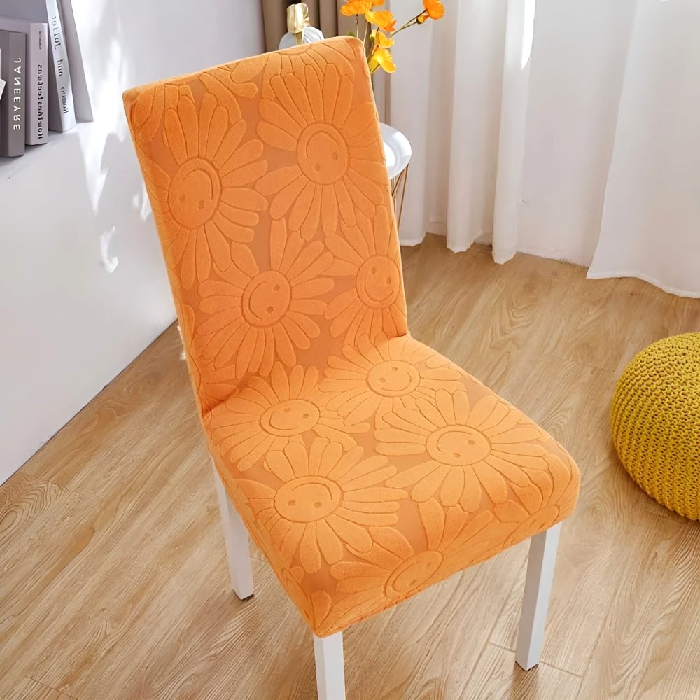 Sunburst Orange Blossom Aura stretch chair cover featuring a floral daisy pattern with smiling faces on a white-legged chair in a home setting.