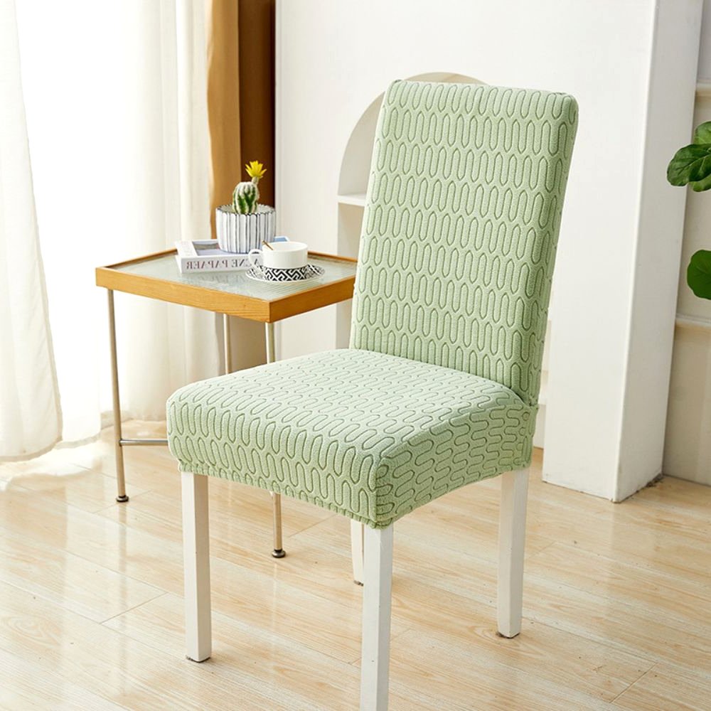 Salbeigrüner elastischer Jacquard-Stuhlbezug mit Chevron-Mäandermuster, gezeigt auf einem Esszimmerstuhl in einem modernen Raum mit Beistelltisch und Pflanze.