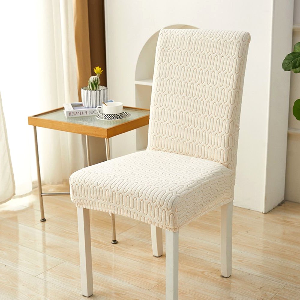 Weißer elastischer Jacquard-Stuhlbezug mit Chevron-Mäandermuster, gezeigt auf einem Esszimmerstuhl in einem modernen Raum mit Beistelltisch und Pflanze.
