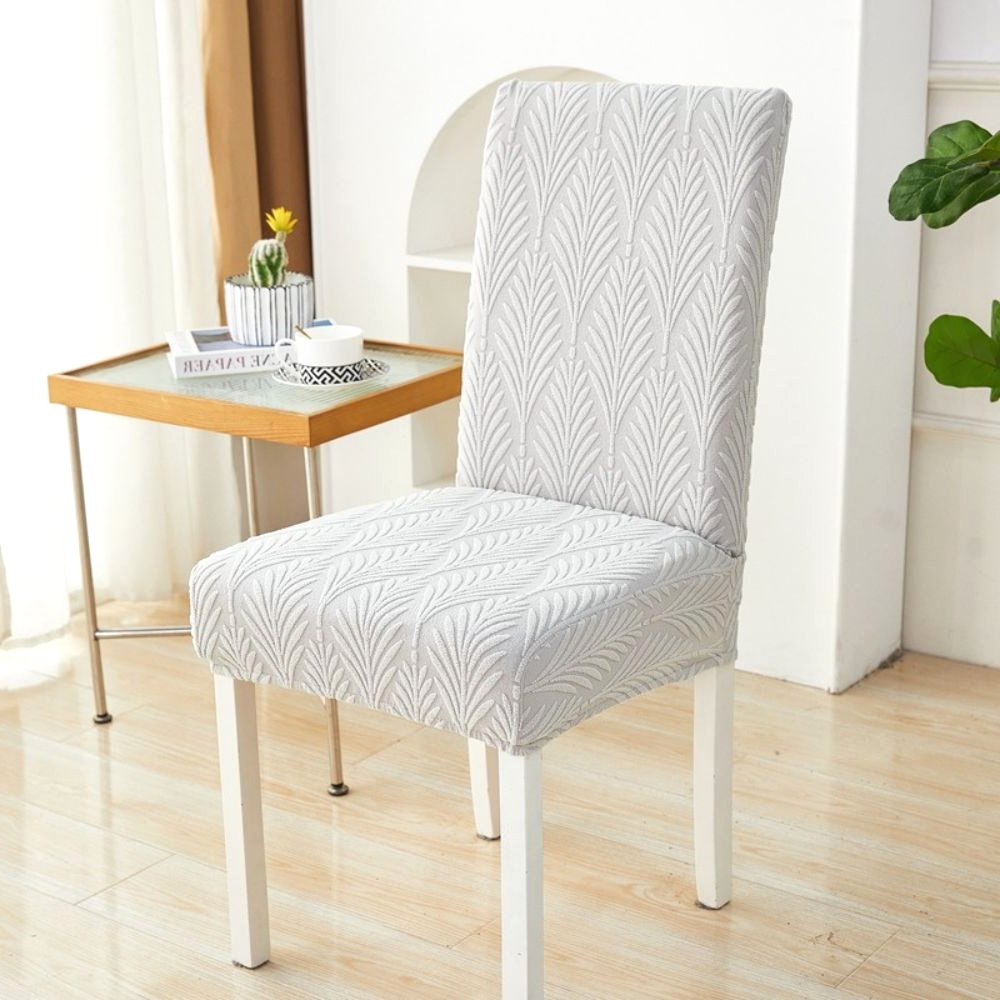 Velvet Haven elastischer Jacquard-Stuhlbezug in Softweiß mit Palmenwebemuster, gezeigt auf einem weißen Esszimmerstuhl. Dieser dehnbare Möbelschoner bietet modernes Design und einfache Montage.