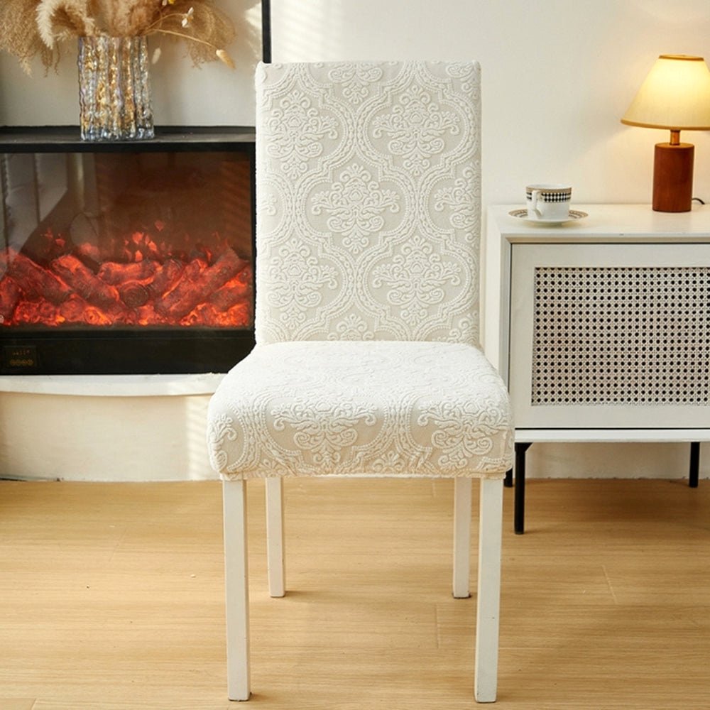 Elegant cream jacquard chair seat slipcover on a dining chair in a living room setting with a fireplace and side table.